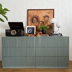 a blue and white dresser with pictures on it next to a plant in a vase