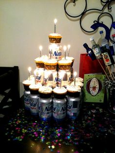 a cake made out of cupcakes with lit candles on top is surrounded by cans