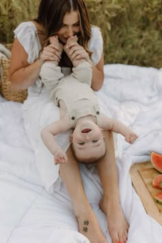 a woman laying on top of a bed next to a baby in her lap and eating watermelon