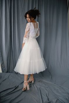 a woman is standing in front of a gray backdrop wearing a white dress and heels