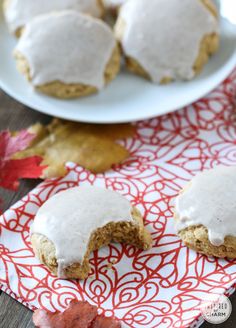 some frosted donuts are on a red and white napkin next to a plate with leaves