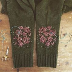 a pair of green gloves sitting on top of a wooden floor next to scissors and thread