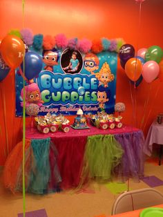 a table topped with balloons and cake next to a bubble gupple sign on a wall