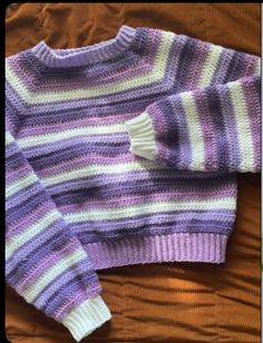 a purple and white sweater sitting on top of a bed