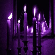 three candles are lit in front of a mirror with purple lights on it and one candle is glowing