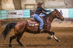 a woman riding on the back of a brown horse in an arena at a rodeo