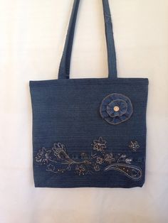 a denim bag with embroidered flowers on the front and side, hanging from a hook