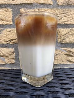 a glass filled with liquid sitting on top of a table next to a brick wall