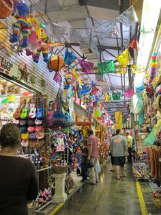 people are walking through an open market with lots of items hanging from the ceiling and in front of them