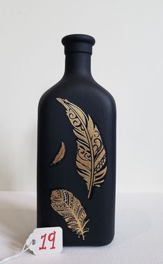 a black bottle with gold feathers painted on it