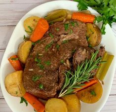 a white plate topped with meat, potatoes and carrots next to some parsley