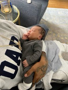 a man holding a sleeping baby on top of a couch next to a glass table