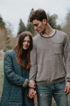 a man and woman holding hands while standing next to each other in front of trees