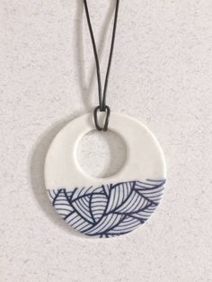 a white and blue ceramic pendant hanging from a black cord on a gray surface with an oval design in the center