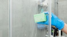 a person in blue gloves and rubber gloves cleaning a glass door with a sponge on it