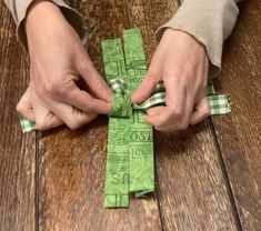 two hands are tying the ends of a green ribbon on a wooden table with wood flooring