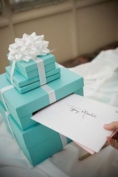 a stack of blue gift boxes sitting on top of a bed next to a note