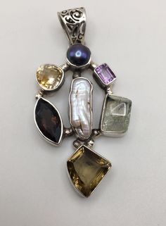 Beautiful designed - multi shapes and 7 gemstones on the 925 silver holder Pendant with round clasp. The pendant mix of Amethyst, Green Quartz, Citrine and Smoky Quartz, Mother of Pearl. Good pre-own condition. It stamped "925" on the silver holder.  Pendant Size: 2 3/4" (H) x 1 3/8" (W) (6 cm x 3.5 cm) with the top clasp. Weight:  23 grams (0.7 Troy Ozs)  Item is exactly as shown in pictures.   Please carefully review the item description and accompanying pictures before making a purchase, as w Elegant Multi-stone Gemstones In Sterling Silver, Elegant Multi-stone Sterling Silver Gemstones, Elegant Multistone Sterling Silver Gemstones, Sterling Silver Fusion Style Natural Gemstones, Spiritual Silver Multi-stone Gemstones, Sterling Silver Gemstones With Natural Stones For Anniversary, Sterling Silver Multi-stone Round Pendant Jewelry, Unique Sterling Silver Gemstones With Accents, Unique Sterling Silver Gemstones