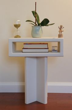 a white table topped with books and a vase filled with flowers next to a wall