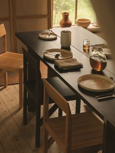 the table is set with plates, cups and utensils in front of an open window