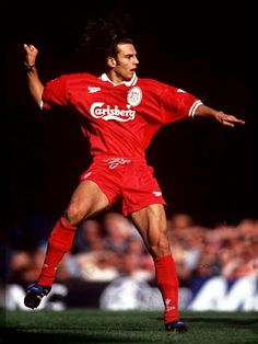 a man in red uniform kicking a soccer ball with his arms out to the side