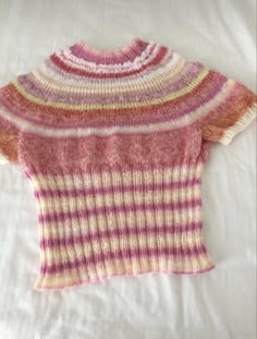 a pink and yellow sweater is laying on a white bed with the words knitted by