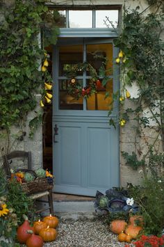 a blue front door with pumpkins and gourds in the garden next to it