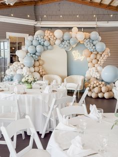 a room filled with tables covered in white and blue balloon decorations, chairs and table cloths