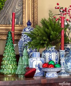 a table topped with blue and white vases filled with christmas decorations next to a painting