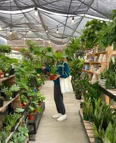 a woman is looking at plants in a greenhouse with lots of potted plants on the shelves