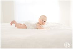 a baby laying on top of a bed in a white dress and smiling at the camera