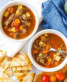 two bowls of beef stew with carrots, celery and bread on the side