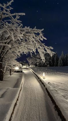 a snow covered road at night with street lights on the side and trees in the background