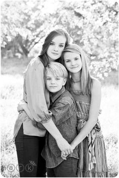 black and white photograph of three girls hugging each other in front of a field with trees