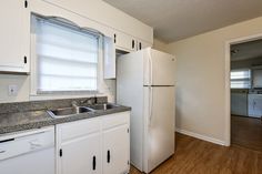 an empty kitchen with white cabinets and granite counter tops in front of a refrigerator freezer