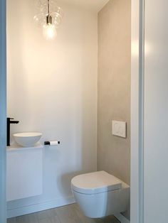 a white toilet sitting in a bathroom next to a sink and light fixture on the wall