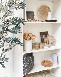 a white shelf filled with baskets and other items next to a potted olive tree