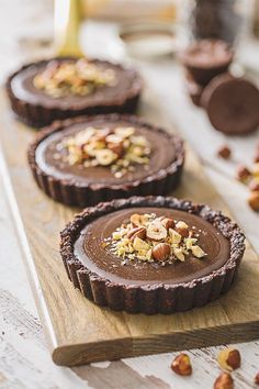 three chocolate tarts with nuts on top and some other desserts in the background