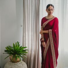 a woman in a red sari standing next to a potted plant and window