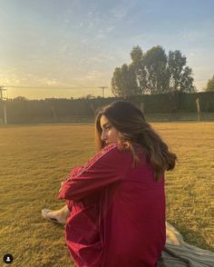 a woman sitting on top of a wooden bench next to a lush green field under a blue sky