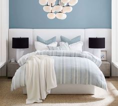 a bedroom with blue walls, white bedding and a chandelier hanging from the ceiling