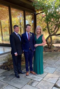 three people standing next to each other in front of a building with glass walls and trees