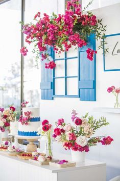 a table topped with lots of cakes and flowers next to blue shutters on the wall