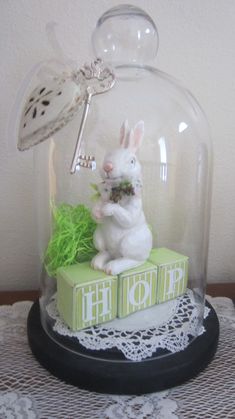 a white rabbit sitting on top of a green box under a glass dome