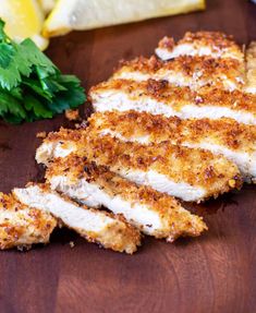 some chicken on a cutting board with parsley and lemon wedges next to it