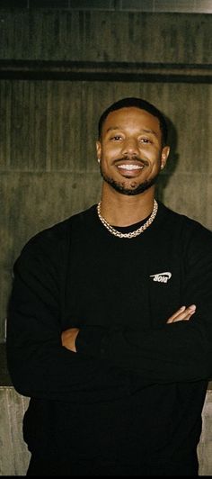 a man standing in front of a wall with his arms crossed and smiling at the camera