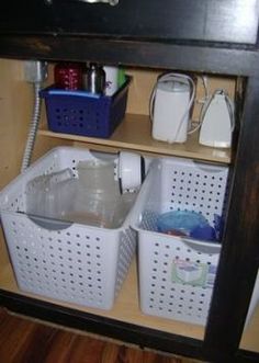 two white baskets under a black shelf with other items on it and one blue basket underneath the shelf