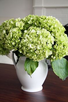 a white vase filled with green flowers on top of a wooden table