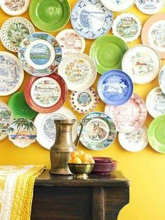 plates are arranged on the wall in front of a table with fruit and a vase