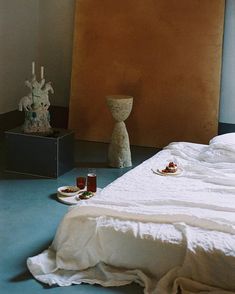 a bed sitting in a bedroom next to a table with food on it and two vases